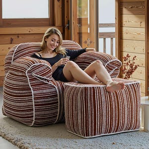 May include: A large, comfortable armchair and matching footstool set. The furniture features a brown and white striped pattern with white piping. The chair has a rounded shape and is designed for relaxation. The footstool is a cube shape.