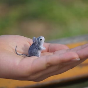 May include: A small gray and white needle felted mouse figurine sitting in the palm of a hand.