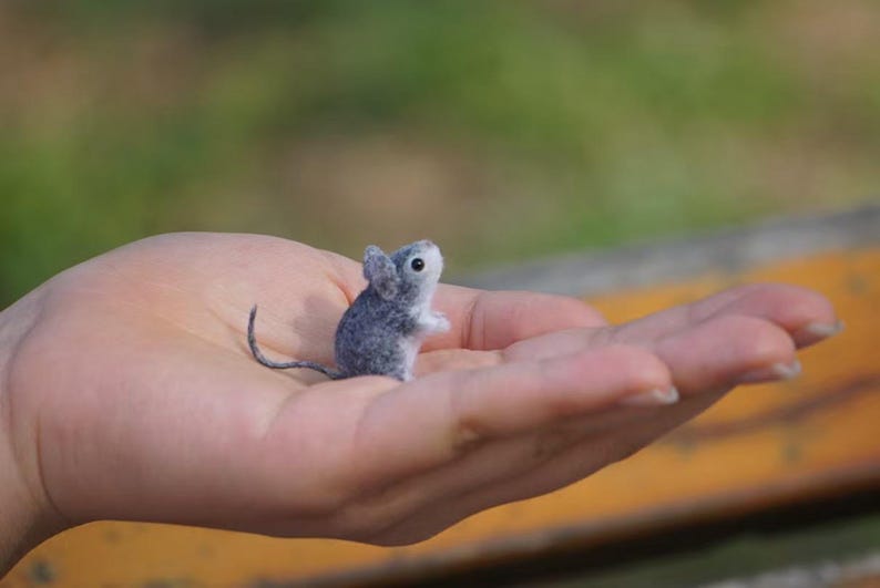 May include: A small gray and white needle felted mouse figurine sitting in the palm of a hand.