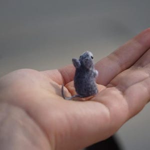 May include: A small gray felt mouse figurine sitting in the palm of a hand.