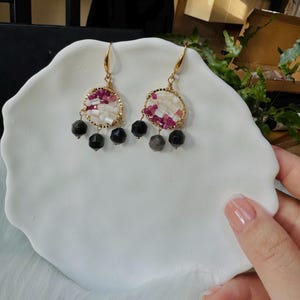 Puede incluir: Un par de pendientes de oro con detalles de mosaico de concha rosa y blanca y gotas de piedras preciosas negras.