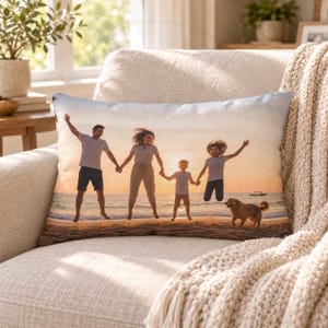 May include: A rectangular throw pillow featuring a printed photograph of a family of four and a dog jumping on a sandy beach at sunset. The scene includes two adults and two children silhouetted against the bright orange and yellow sky.