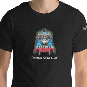 Peut inclure: T-shirt gris foncé avec un motif de train de dessin animé bleu, rouge et argenté, avec le texte "TACTICAL CHOO CHOO" en dessous. Le t-shirt a un col rond et des manches courtes. Le design a un thème tactique.