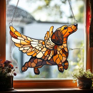 May include: Stained glass dachshund with wings, in shades of brown, orange, and yellow. The dog is suspended by a chain, designed to hang in a window. The wings are spread, and the dog appears to be in flight. A unique home decor item.