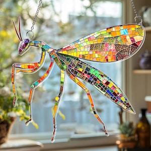 May include: A colorful stained glass praying mantis suncatcher. The insect features a mosaic design with vibrant hues of red, orange, yellow, green, and blue. It hangs from a silver chain, perfect for window or wall decor.