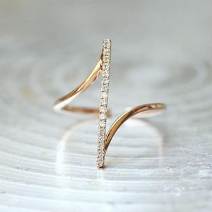 May include: A rose gold ring with a vertical row of small, clear gemstones. The ring has a unique open design with curved bands that wrap around the finger. The gemstones sparkle against the warm metal.