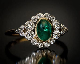 May include: A vintage emerald and diamond ring with a green oval emerald gemstone surrounded by a halo of small round diamonds. The ring is set in yellow gold.