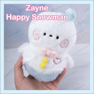 May include: White plush snowman toy with pink bow, yellow buttons, and a red heart on its chest. The snowman has a blue and white hat and is holding a blue and white ball.