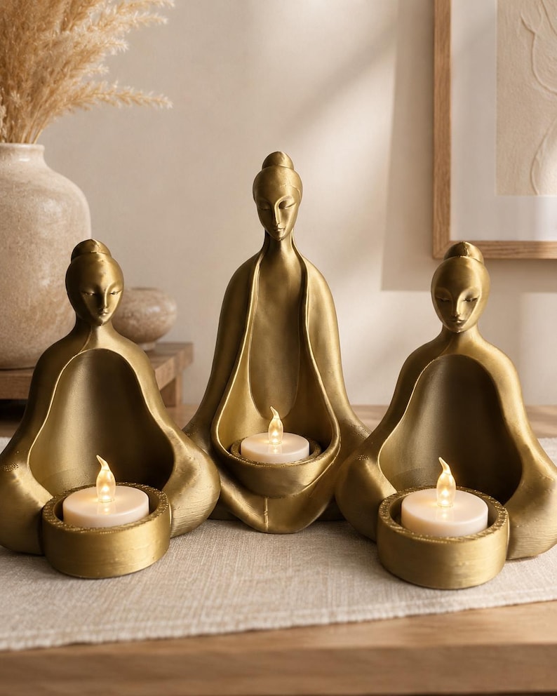 Three brass-finish meditating figures each cradling a lit tea light on a warm shelf