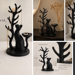 May include: A matte black jewellery organiser featuring a cat figure sitting next to a tree-shaped stand with multiple branches for necklaces and a small circular tray for rings. The base measures 140mm wide, 95mm deep, and 180mm in height.
