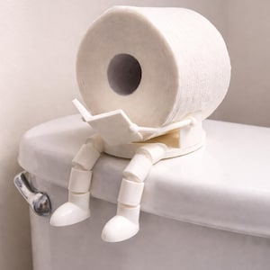 May include: A white toilet paper holder shaped like a seated figure with articulated legs and arms. The figure is constructed from white plastic components and is designed to hold a single roll of white toilet paper in its lap while sitting.