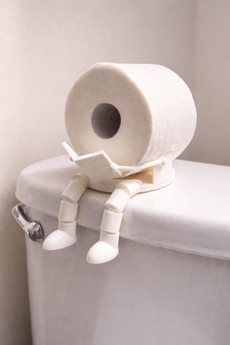 White 3D printed figure with jointed legs sitting on a toilet tank, reading, holding a paper roll