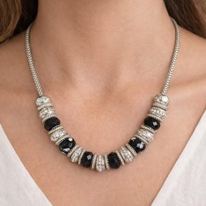 May include: A silver-toned necklace featuring alternating black faceted beads and silver-toned, rhinestone-studded spacers. The necklace has a delicate chain and is worn around the neck. The jewelry is a statement piece.