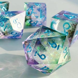 May include: A set of iridescent resin dice in various geometric shapes. The dice have teal blue numbering and a mix of purple, green, and white internal designs. Suitable for tabletop gaming.