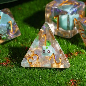 May include: Four clear dice with gold trim and a green frog design. The dice are on a bed of green grass.