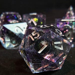 Op de afbeelding: Een set iriserende dobbelstenen met zilveren nummers. De dobbelstenen zijn gemaakt van helder hars met een paars en zwart swirl-patroon. De dobbelstenen zijn perfect voor tabletop gaming.