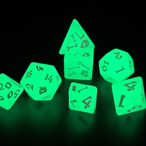 May include: Glow-in-the-dark dice set for tabletop games. The set includes seven dice in various shapes, including a d20, d12, d10, d8, d6, and a unique pyramid-shaped die. Each die is a vibrant green color and features white numbering and skull and crossbones symbols.