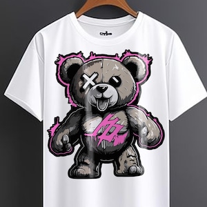 Peut inclure: T-shirt blanc avec un imprimé graphique d'un ours en peluche de dessin animé avec des accents roses. L'ours a une expression espiègle, un œil est couvert d'un X et l'autre œil est ombragé de noir. L'ours porte une chemise rose et blanche avec un imprimé graphique de crâne et d'os croisés.