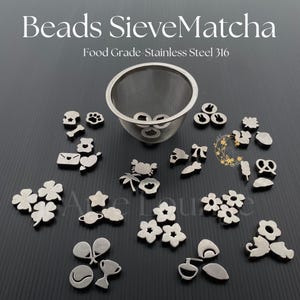 May include: Stainless steel tea sieve with various small, decorative metal charms. Charms include flowers, clovers, stars, and other shapes. The text "Beads SieveMatcha" and "Food Grade Stainless Steel 316" are visible.