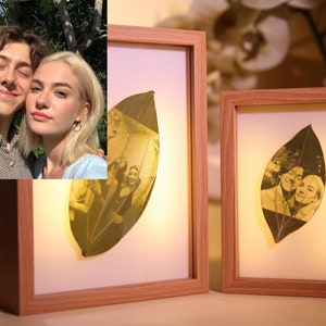 Peut inclure: Deux photographies encadrées d'un couple, chaque photo est imprimée sur une feuille séchée, les cadres sont en bois et ont une finition brun clair.