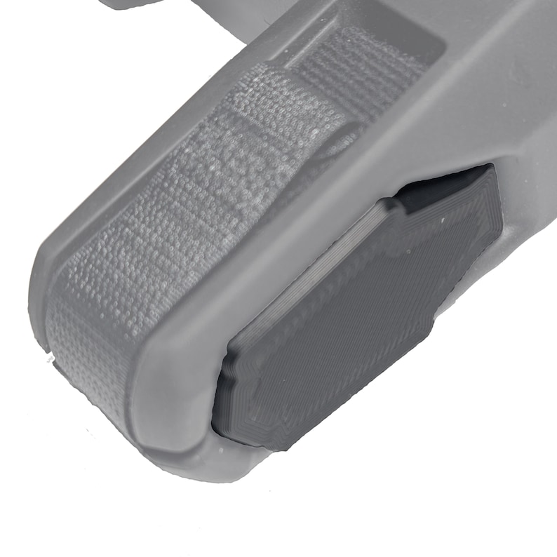 May include: Close-up of a gray plastic component with a textured strap and a dark gray rectangular section. The component has rounded edges and appears to be part of a larger mechanism or device.
