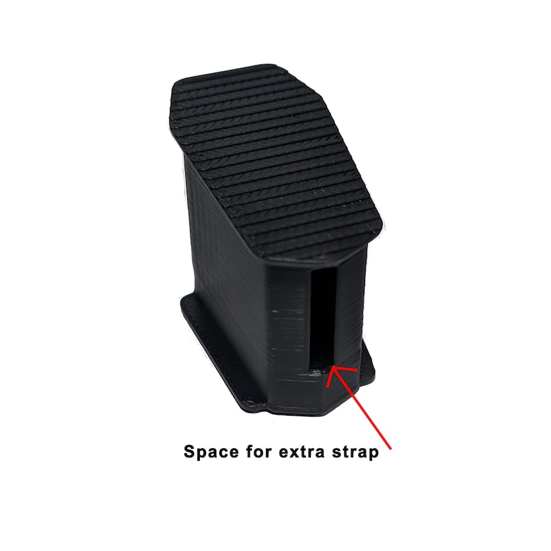 May include: A black, rectangular 3D-printed object with a textured top and a slot. The text "Space for extra strap" is visible below the object. The object appears to be a component or accessory.