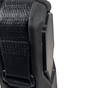 May include: Close-up of a black, textured object with a strap and a curved edge. The object appears to be made of durable materials, with a focus on its construction and design. The image is well-lit, highlighting the details of the object.