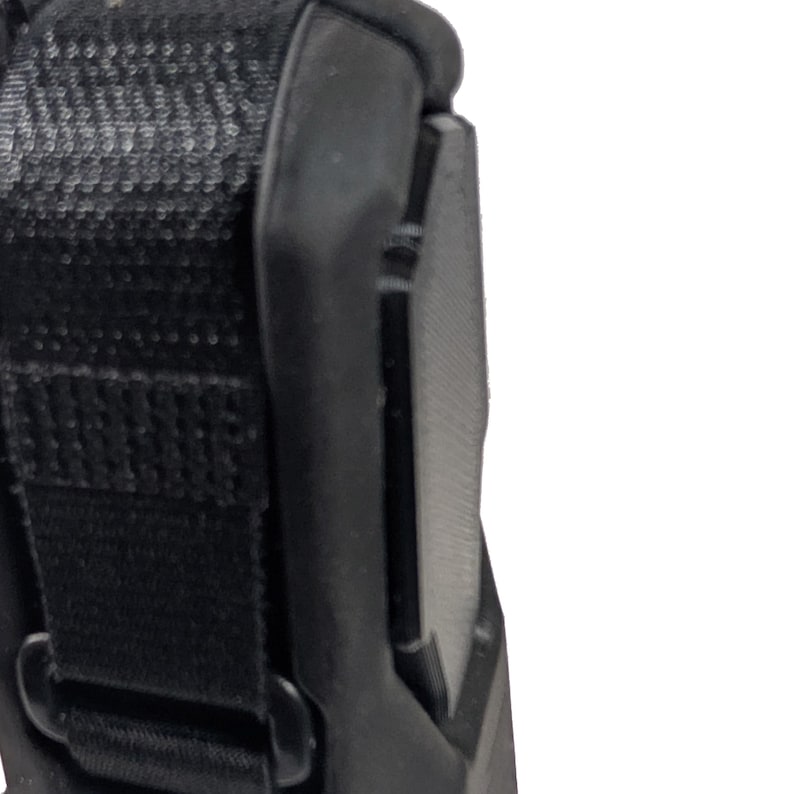 May include: Close-up of a black, textured object with a strap and a curved edge. The object appears to be made of durable materials, with a focus on its construction and design. The image is well-lit, highlighting the details of the object.