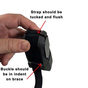 May include: A black brace with a velcro strap and buckle. The text on the image reads, "Strap should be tucked and flush" and "Buckle should be in indent on brace."