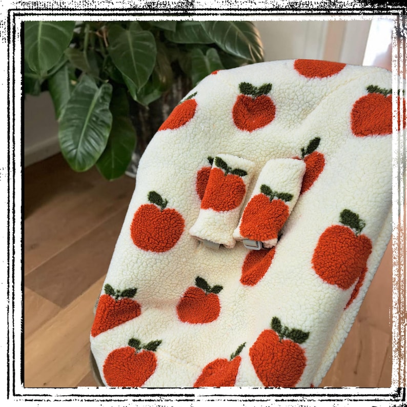Puede incluir: Una funda de asiento de beb&eacute; de felpa color crema con un patr&oacute;n repetido de manzanas rojas con hojas verdes. Tambi&eacute;n se ven dos fundas de correas a juego. La funda est&aacute; dise&ntilde;ada para un asiento de beb&eacute;.