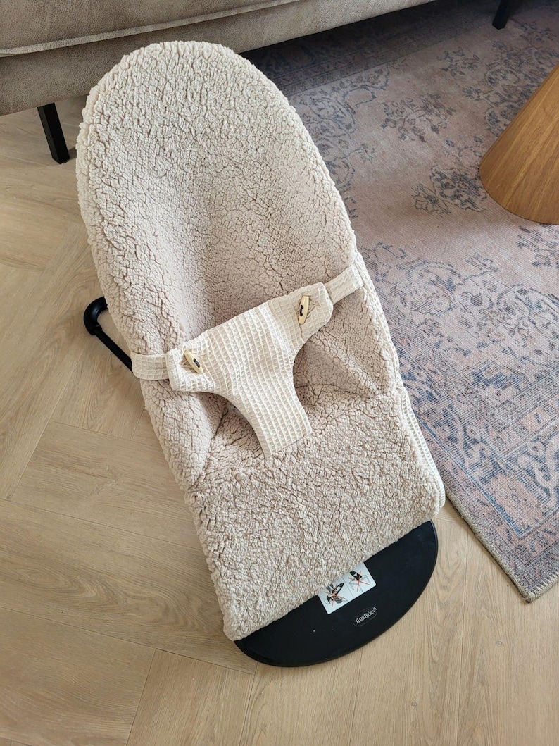 Puede incluir: Un balanc&iacute;n para beb&eacute; beige con un asiento de felpa texturizada y un arn&eacute;s de seguridad de tejido de gofre. El balanc&iacute;n tiene una base negra y un marco negro. Dise&ntilde;ado para beb&eacute;s y ni&ntilde;os peque&ntilde;os.