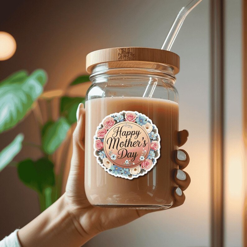 May include: A glass jar with a bamboo lid and a straw. The jar is filled with a light brown liquid and has a sticker on the front that says "Happy Mother's Day" with a floral design.