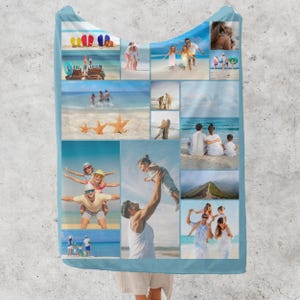 Op de afbeelding: Een lichtblauwe deken met capuchon met een collage van strandvakantiefoto's. De foto's tonen gezinnen, strandtaferelen en zeesterren. De deken is gemaakt van een zacht materiaal.