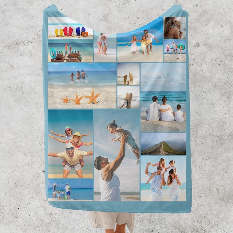 Op de afbeelding: Een lichtblauwe deken met capuchon met een collage van strandvakantiefoto's. De foto's tonen gezinnen, strandtaferelen en zeesterren. De deken is gemaakt van een zacht materiaal.