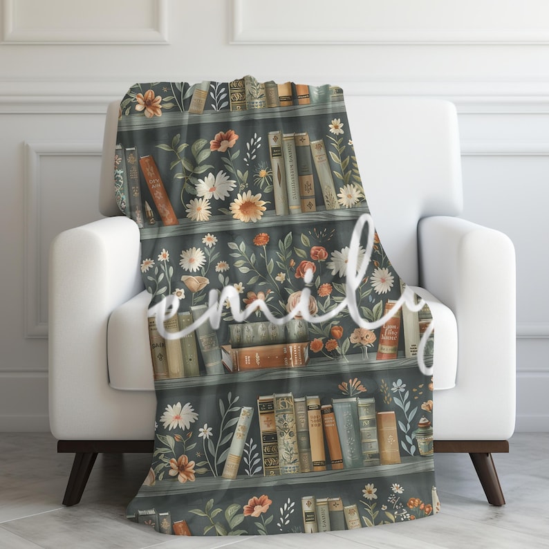 May include: A soft, plush throw blanket featuring a vintage-inspired design of a bookshelf filled with books and flowers. The bookshelf is painted in a dark green color, and the books are a mix of brown, red, and yellow. The flowers are a mix of white, pink, and yellow.