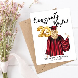 Puede incluir: Tarjeta de graduaci&oacute;n con un globo dorado n&uacute;mero 23, una mujer con una toga de graduaci&oacute;n roja y el texto "Congrats Kayla!" y "University of Alabama Class of 2023".