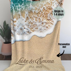 May include: A personalized beach-themed fleece blanket with a wave design and the text "Luke & Emma EST. 2025" printed on it.