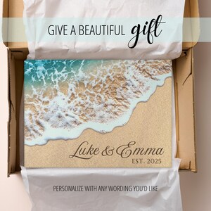 K&ouml;nnte beinhalten: Ein personalisiertes Schneidebrett mit einer Strandszene, die eine Welle zeigt, die auf den Sand trifft. Der Text "Luke & Emma EST. 2025" ist auf das Brett gedruckt.