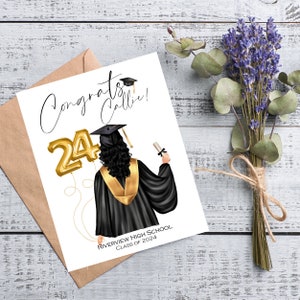 May include: A graduation card with the words "Congrats Callie!" and a graphic of a graduate in a black gown and gold stole, holding a diploma. Gold "24" balloons are featured. The card is on a wooden surface with a bouquet of lavender.