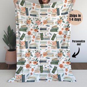 May include: A white fleece blanket with a repeating pattern of stacked books and flowers. The name "Jenna" is repeated throughout the pattern.