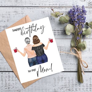 May include: A birthday card with the text "Happy Birthday to my Mom!" features an illustration of two women holding mugs. The card is next to a brown envelope and a bundle of lavender and eucalyptus tied with twine.