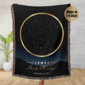 May include: A black woven throw blanket with a gold circle design featuring a constellation of stars. The text "Mark & Evelyn" and "February 14, 2024" is printed below the circle.