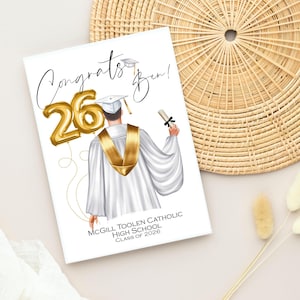May include: A graduation card with the words "Congrats Ben!" and a gold foil balloon that reads "26". The illustration shows a graduate in a white gown and gold sash. The card also includes the text "McGill Toolen Catholic High School Class of 2026."