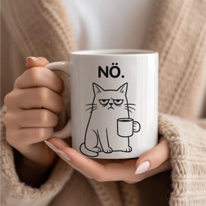 Könnte beinhalten: Weiße Keramiktasse mit einer schwarzen Illustration einer grummeligen Katze, die eine Kaffeetasse hält. Über der Katze steht das Wort "NÖ.". Die Tasse wird von einer Person gehalten. Perfekt für Kaffee oder Tee.