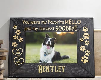 May include: Black wooden photo frame with a gold inscription that reads "You were my favorite hello and my hardest goodbye". The frame has gold paw prints and hearts with the years 2008 and 2022. The frame has a photo of a black and white dog named Bentley.