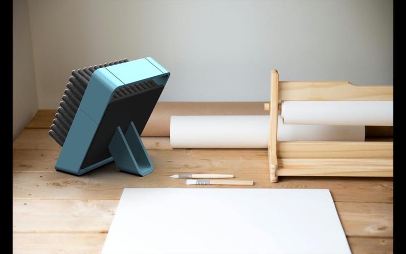 May include: A light blue brush holder with a black base and a stand. The brush holder is filled with a variety of brushes. The brush holder is sitting on a wooden table.