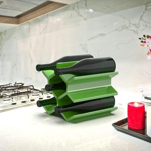 May include: A green metal wine rack with six bottles of wine. The rack is on a white countertop in a kitchen.