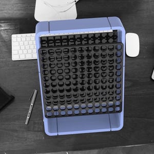 May include: A blue plastic organizer with a black gridded tray. The tray has many small compartments for holding small items.