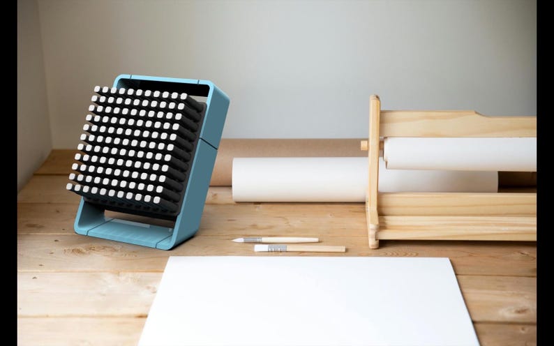May include: A light blue fan with a black grid of small squares. The fan is sitting on a wooden surface with a white sheet of paper and a wooden paper roll holder.