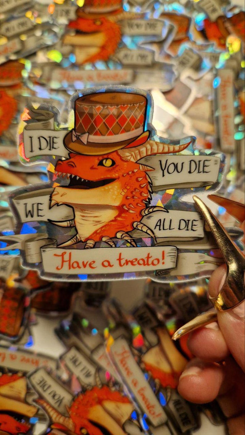 Może przedstawiać: Holograficzna naklejka przedstawiająca czerwonego smoka w brązowym i białym kapeluszu w kratkę. Naklejka zawiera tekst "Ja umieram", "Ty umierasz", "My wszyscy umieramy" i "Weź smakołyk!"